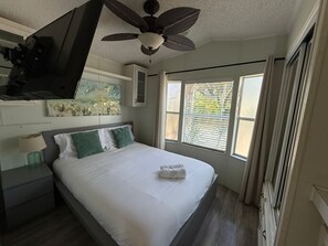 A bedroom with a bed, a nightstand, a ceiling fan, a window with blinds, and a painting on the wall. - The peaceful Lake House (Kissimmee)