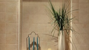Un baño con baldosas color crema, un florero blanco con plantas verdes y un candelabro con velas.