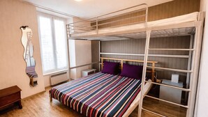 Una camera con letto a castello, una coperta a righe, una piccola panca di legno e una finestra con tende.