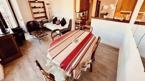 Un ambiente compatto con tavolo da pranzo, sedie, divano, angolo cottura e un'ampia finestra.