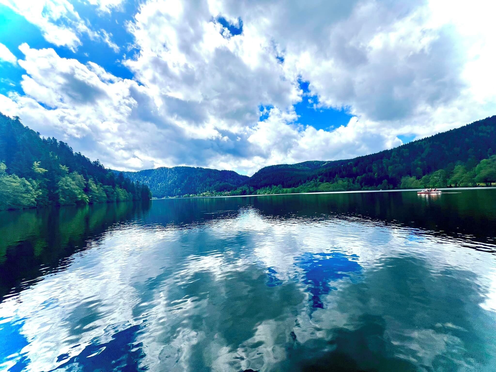 A calm lake with reflections of the sky and surrounding forest.