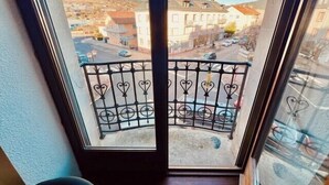 Un balcone con ringhiera in ferro battuto che si affaccia su una strada con edifici e un paesaggio collinare.