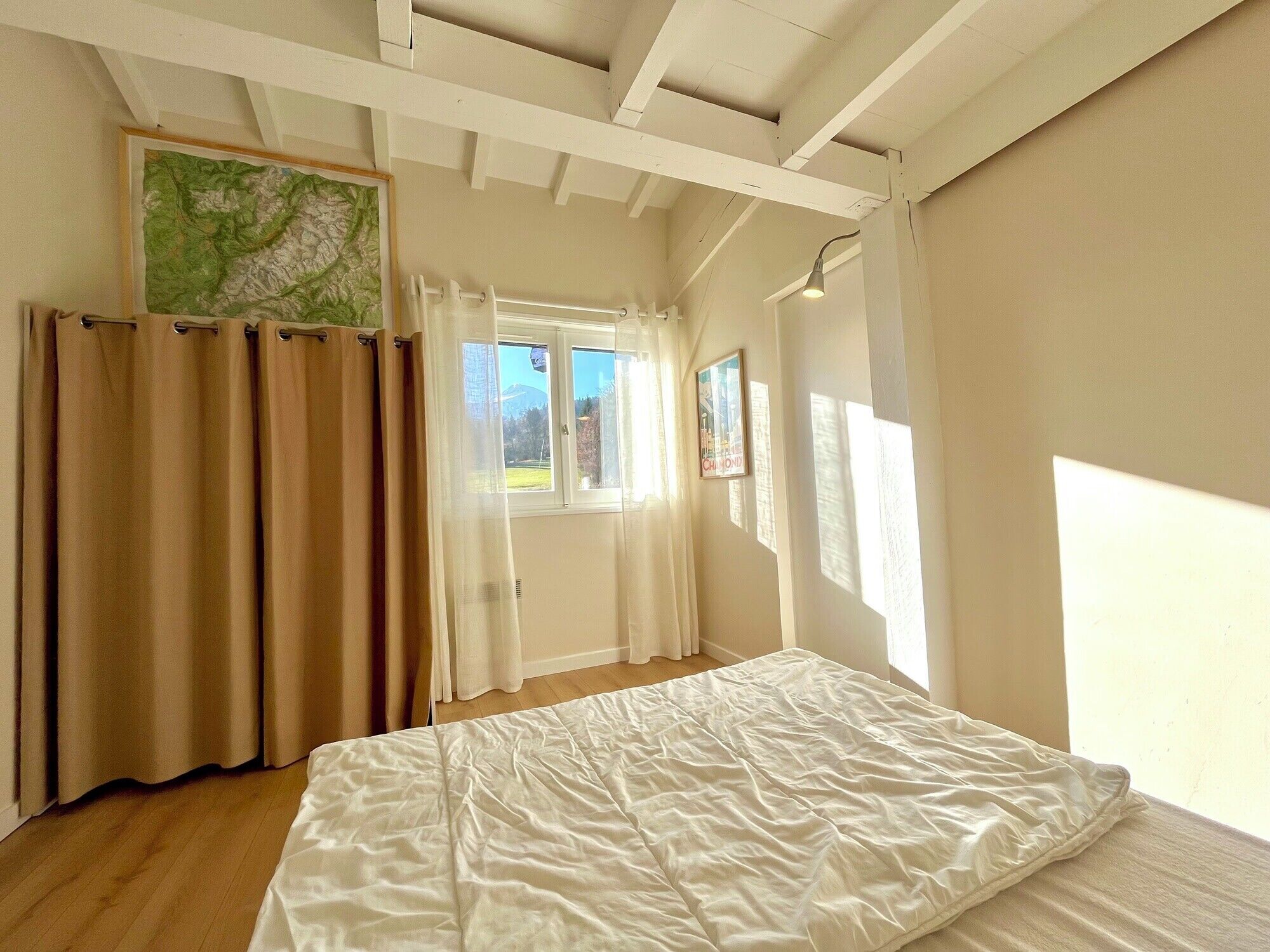 A bedroom with a bed, a window, curtains, and a map on the wall.