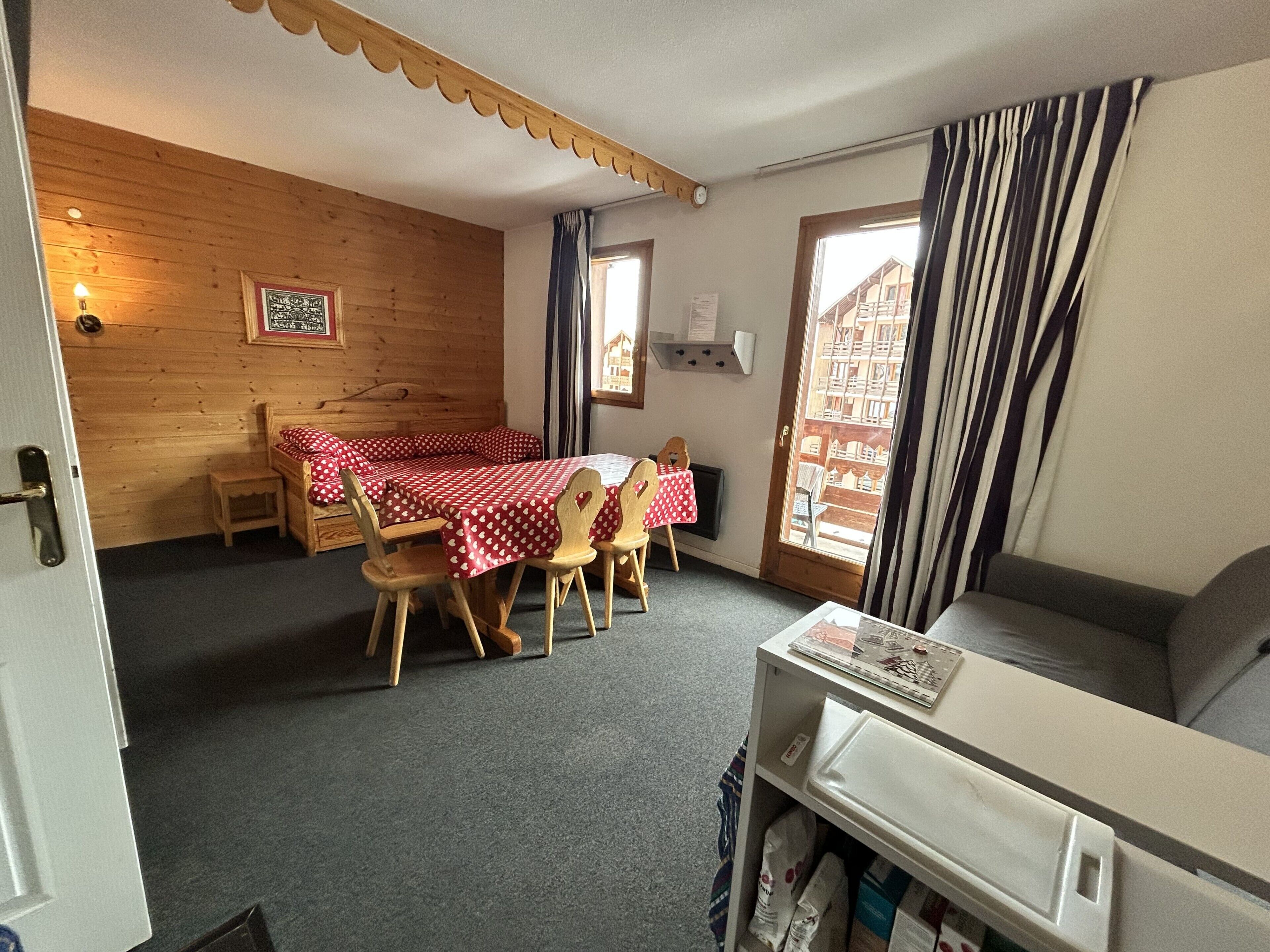 Una habitación acogedora con una pared de madera, una mesa de comedor con mantel a cuadros rojo y blanco, y un sofá.