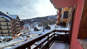 A balcony with a wooden railing overlooking a snowy landscape, featuring buildings and a clear sky. - Bright studio in Risoul, ski on foot and comfort (Risoul)