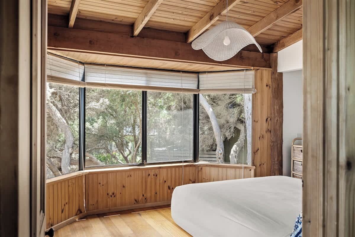 A bedroom with a large window, wooden walls, and a bed.
