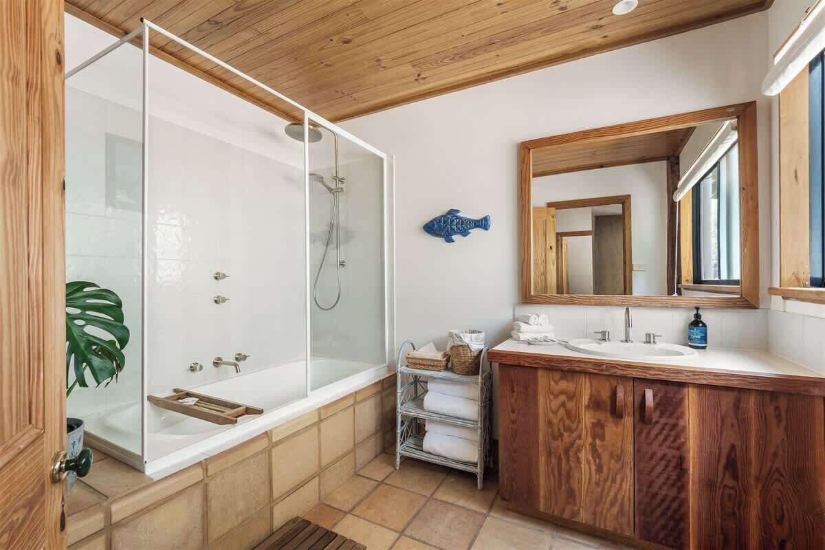 A modern bathroom with a glass-enclosed shower, wooden vanity, and a large mirror.