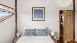 Une chambre à coucher avec un lit, deux lampes de chevet, un tableau encadré au mur, une fenêtre et une porte donnant sur une autre pièce.