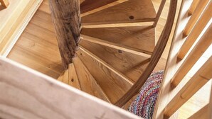 Un escalier en colimaçon en bois, avec une corde enroulée autour d’un poteau, mène à un banc à rayures recouvert de tissu.