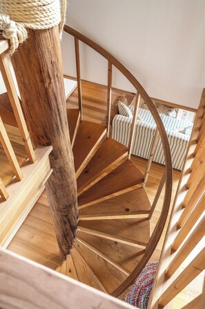 Eine Holzspirale mit einem um einen Pfosten gebundenen Seil, das zu einer gestreiften, gepolsterten Bank führt.