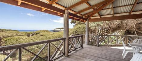 A covered outdoor deck with a view of the ocean, wooden railings, and white plastic chairs.
