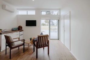 A modern kitchen with a flat-screen TV, wooden chairs, a small table, and a sliding glass door leading to a patio.