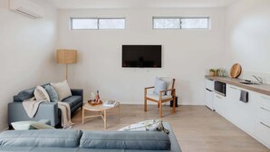 Un saló modern amb un sofà, una butaca, una taula de centre i un televisor de pantalla plana penjat a la paret.