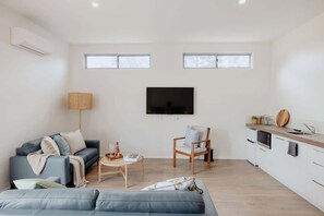 A modern living room with a sofa, armchair, coffee table, and a flat-screen TV mounted on the wall. - Bailey Estate—Margaret River Lakeside Stay (Rosa Brook)