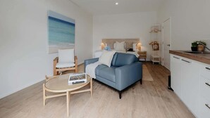 Un saló modern amb un sofà, una taula de centre rodona i un quadre d'una platja.