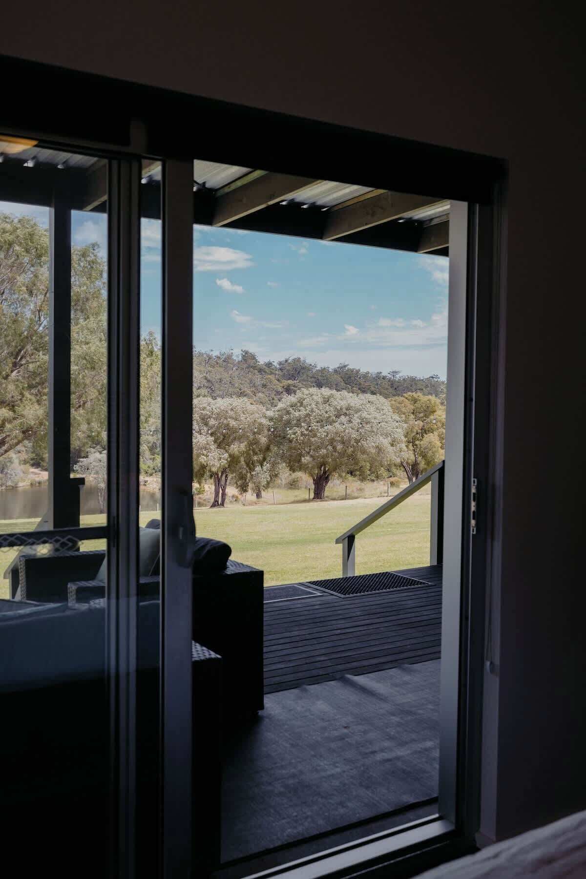Quarto com porta de vidro deslizante que dá para área externa com vista para árvores e um campo gramado.