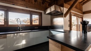A modern kitchen with a large island, stainless steel appliances, and wooden beams. - Chalet Orrana in the heart of Courchevel Village (Courchevel)