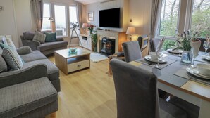 A modern living room with a sofa set, a dining table set for two, a fireplace, and a television mounted on the wall. - Argyll View Lodge (Wemyss Bay)
