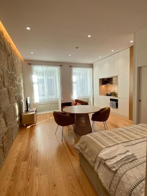 A modern bedroom with a bed, a round dining table with chairs, a stone accent wall, and a kitchen area. - Porto Suites (Porto)