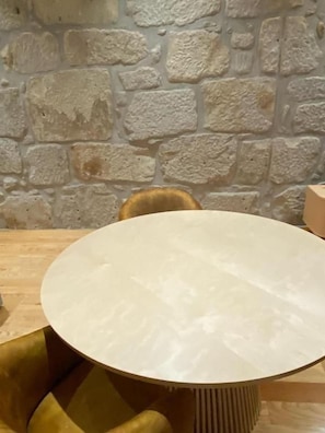 A round table with a light-colored top, positioned in front of a stone wall. - Porto Suites (Porto)
