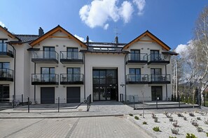 A modern two-story building with balconies, large windows, and a paved entrance area.