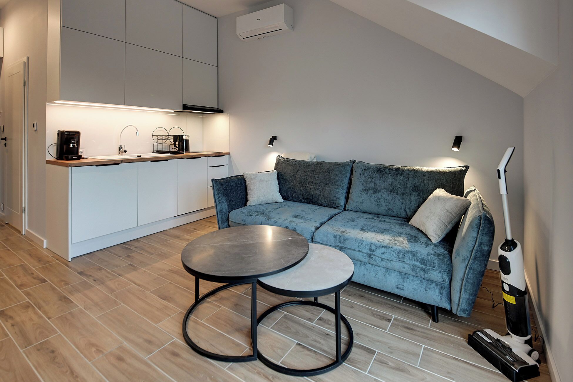 Un espacio habitable compacto con kitchenette, un sofá, una mesa de centro y un aspirador.