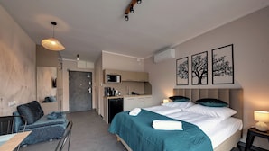 Ein modernes Hotelzimmer mit Bett, Schreibtisch, Sofa, Mikrowelle und einer kleinen Küchenzeile.