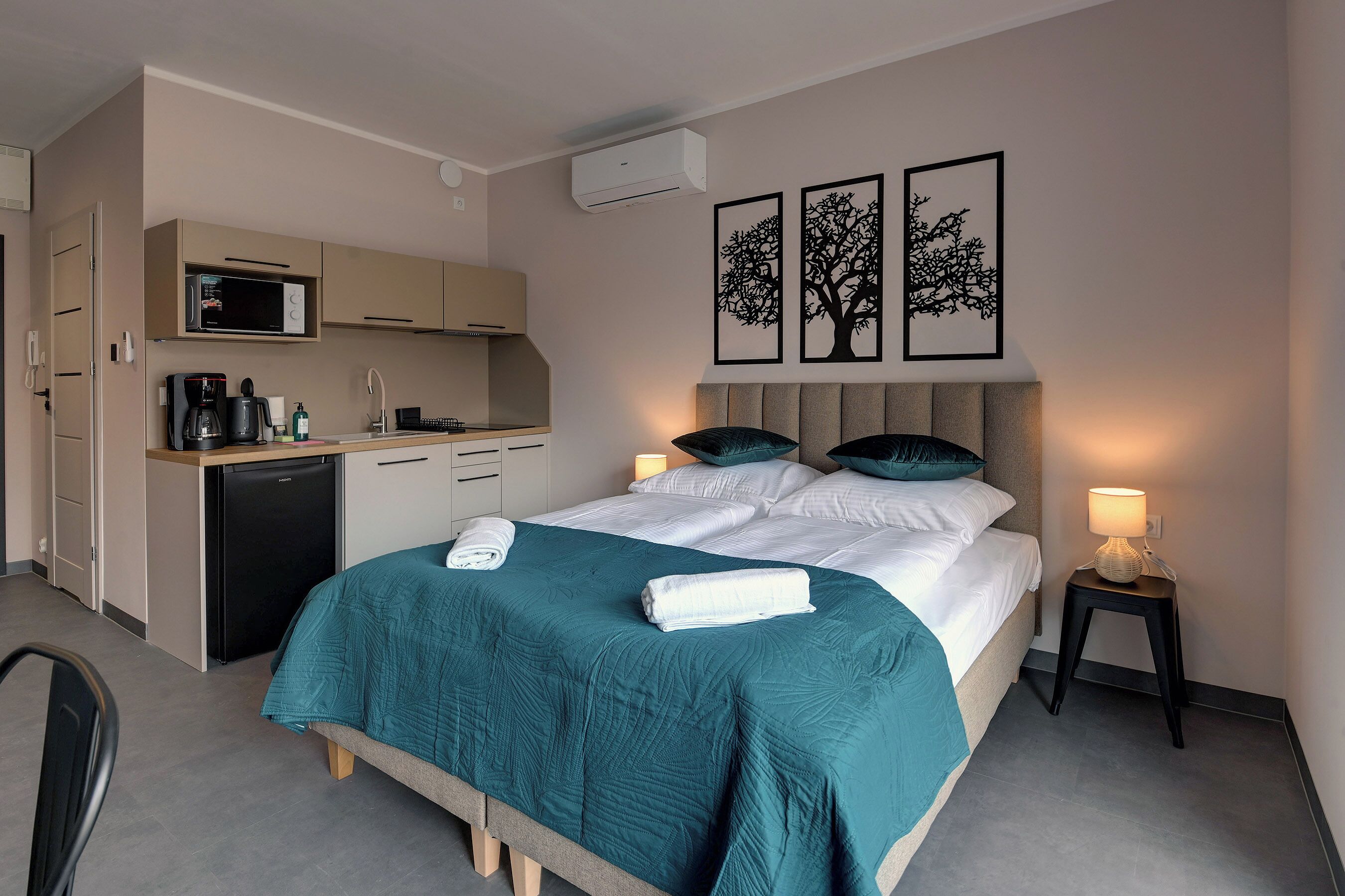 Una habitación de hotel compacta con cama, mesita de noche y zona de kitchenette.