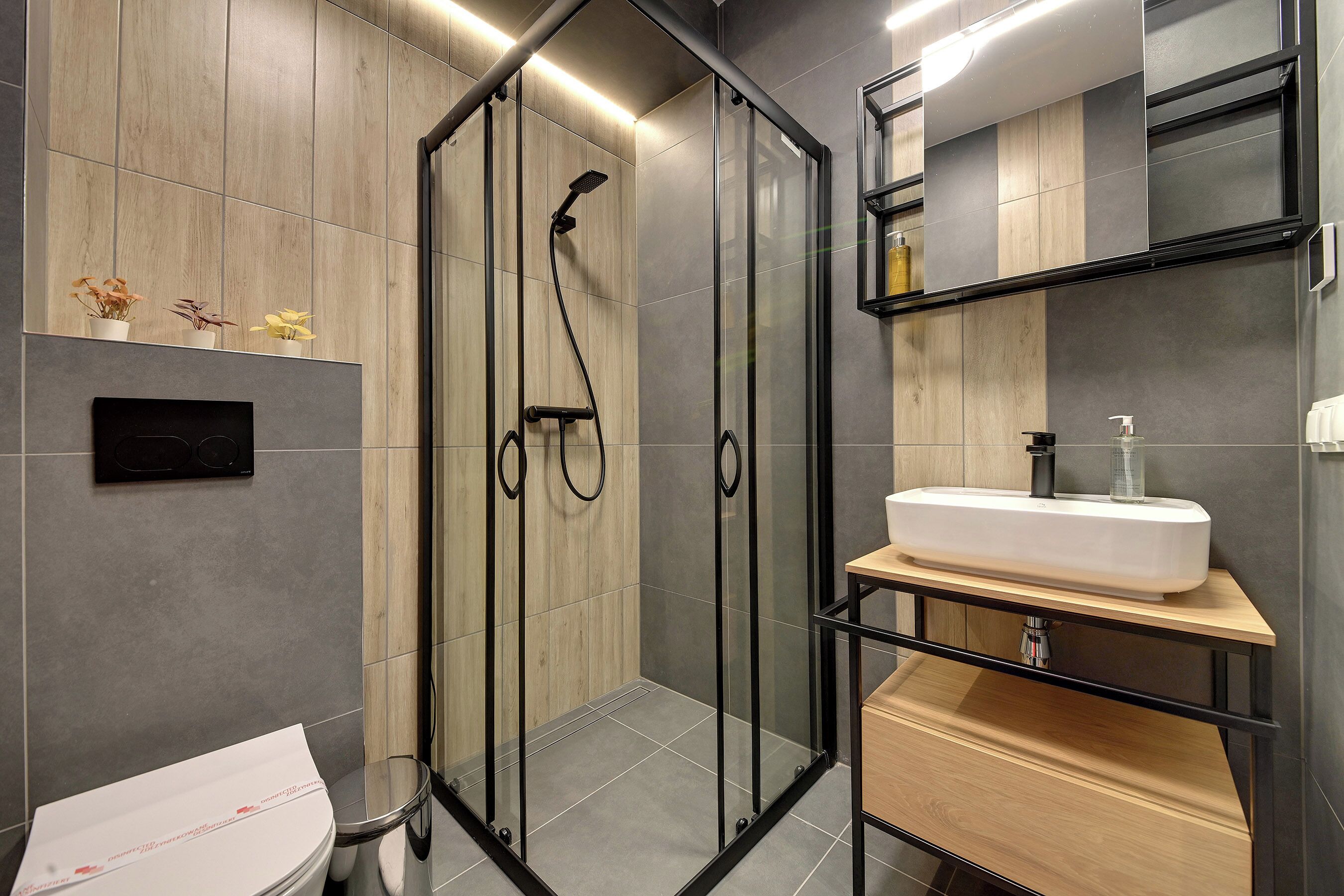 A modern bathroom with a glass-enclosed shower, a white sink, and a wooden vanity.