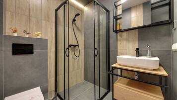 A modern bathroom with a glass-enclosed shower, a white sink, and a wooden vanity.