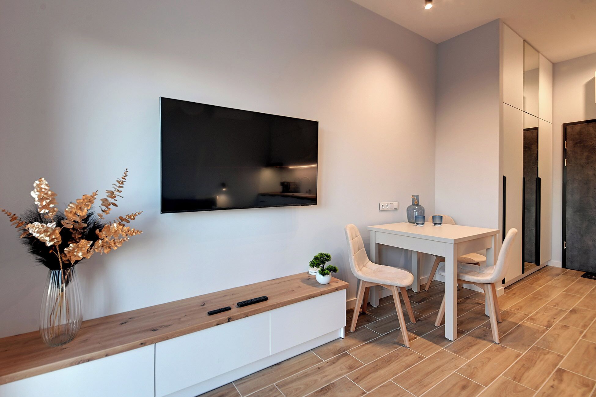 Een moderne keuken met een ingebouwde oven, een eettafel met stoelen en een wit kastje met een houten aanrechtblad.