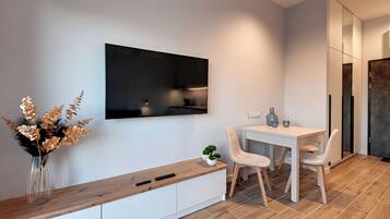 Een moderne keuken met een ingebouwde oven, een eettafel met stoelen en een wit kastje met een houten aanrechtblad.