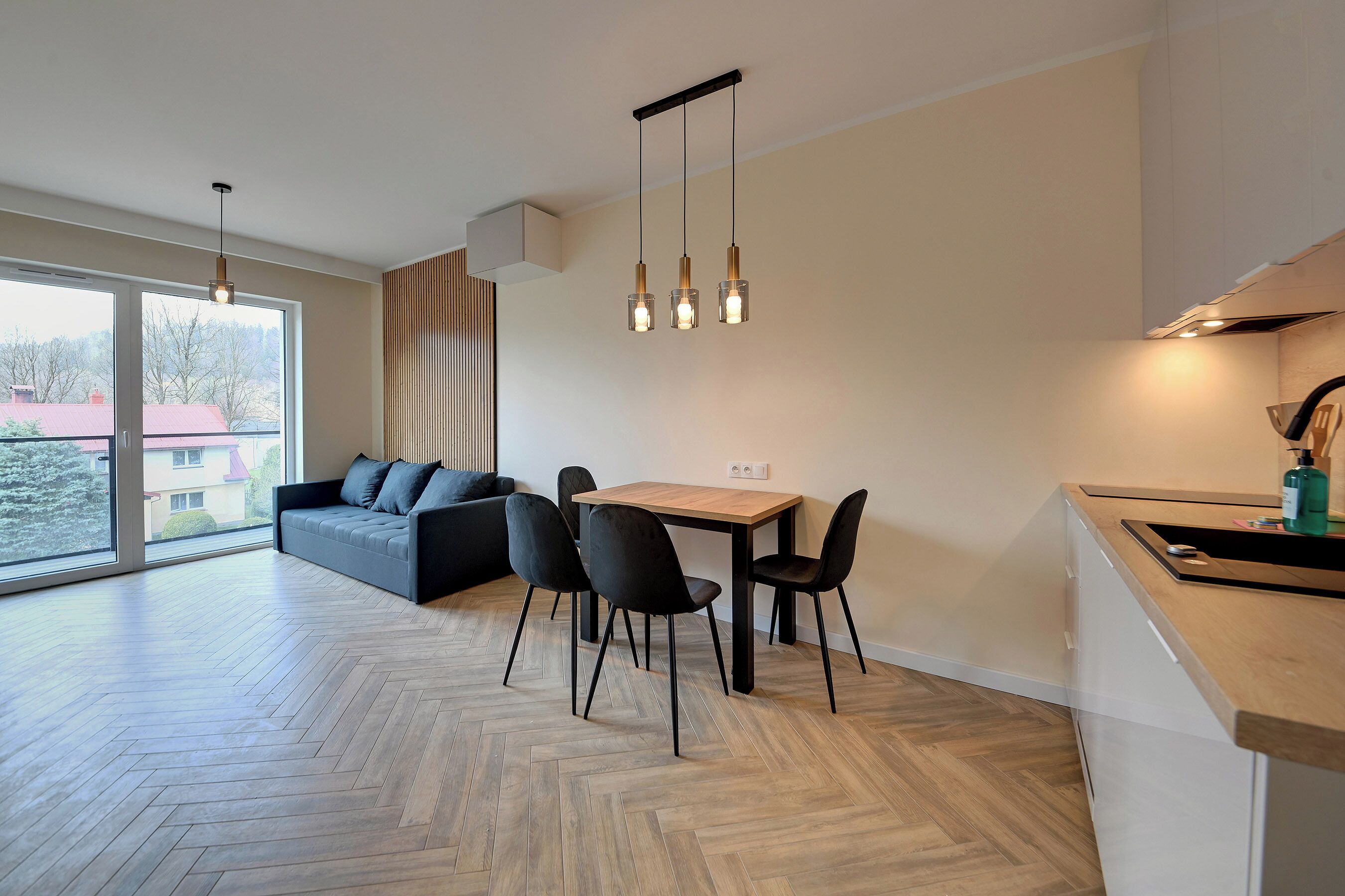 A modern kitchen with a dining area, large windows, and a herringbone wood floor.