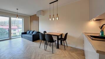A modern kitchen with a dining area, large windows, and a herringbone wood floor.