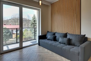 Un salon moderne avec un canapé gris, une grande porte-fenêtre coulissante et un mur composé de lattes de bois.