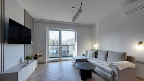 Ein modernes Wohnzimmer mit einer Couch, einem Couchtisch, einem Fernseher und einer großen Glasschiebetür, die auf einen Balkon führt.