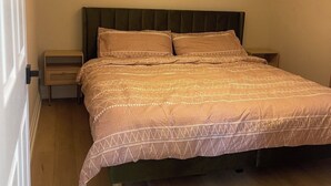 A neatly made bed with a patterned bedspread, a bedside table with a lamp, and an air conditioning unit on the wall. - 1 Bed, 1 Bath Private Bungalow in downtown Thorold (Thorold)