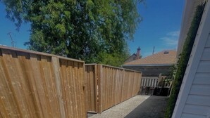 A paved backyard with a wooden fence and a white house. - 1 Bed, 1 Bath Private Bungalow in downtown Thorold (Thorold)
