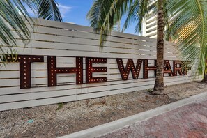 Ein Schild mit beleuchteten Buchstaben, auf dem 'THE WHARF' steht, an einer weißen Wand mit horizontalen Linien.