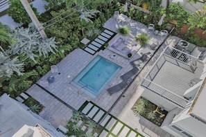 An aerial view of a rooftop with a swimming pool, lounge chairs, and surrounding greenery.