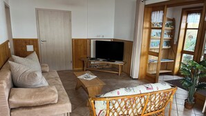 A cozy living room with a sofa, a wooden coffee table, a wicker chair, a television, and a bookshelf. - Cozy vacation apartment on a resettlement farm (Bad Wildungen)