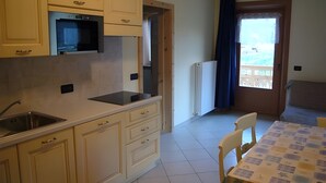 A kitchen with a microwave, sink, and cabinets, a dining area with a table and chairs, and a view through a window. - Apartment '1' with Mountain View, Shared Garden and Wi-Fi (Livigno)