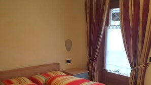 A double bed with striped bedding, a bedside table, a wall-mounted light, and a window with curtains. - Apartment '1' with Mountain View, Shared Garden and Wi-Fi (Livigno)