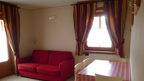 Un sofá rojo, una mesita con mantel a cuadros y una ventana con cortinas.
