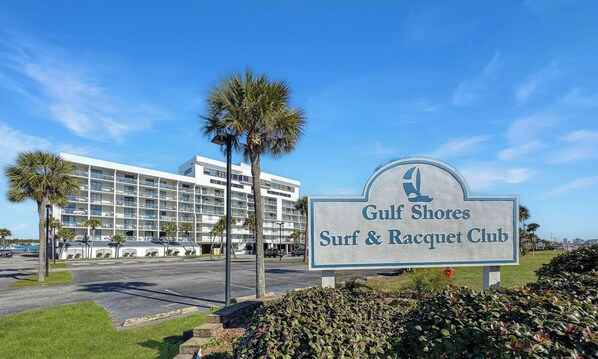 A sign for Gulf Shores Surf & Racquet Club with a modern building in the background. - 1BR Gulf Shores Surf & Racquet | Free Activities (Gulf Shores)