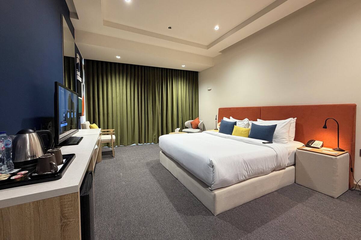 Een hotelkamer met een bed, nachtkastje en een bureau met een computer en koffiezetapparaat.