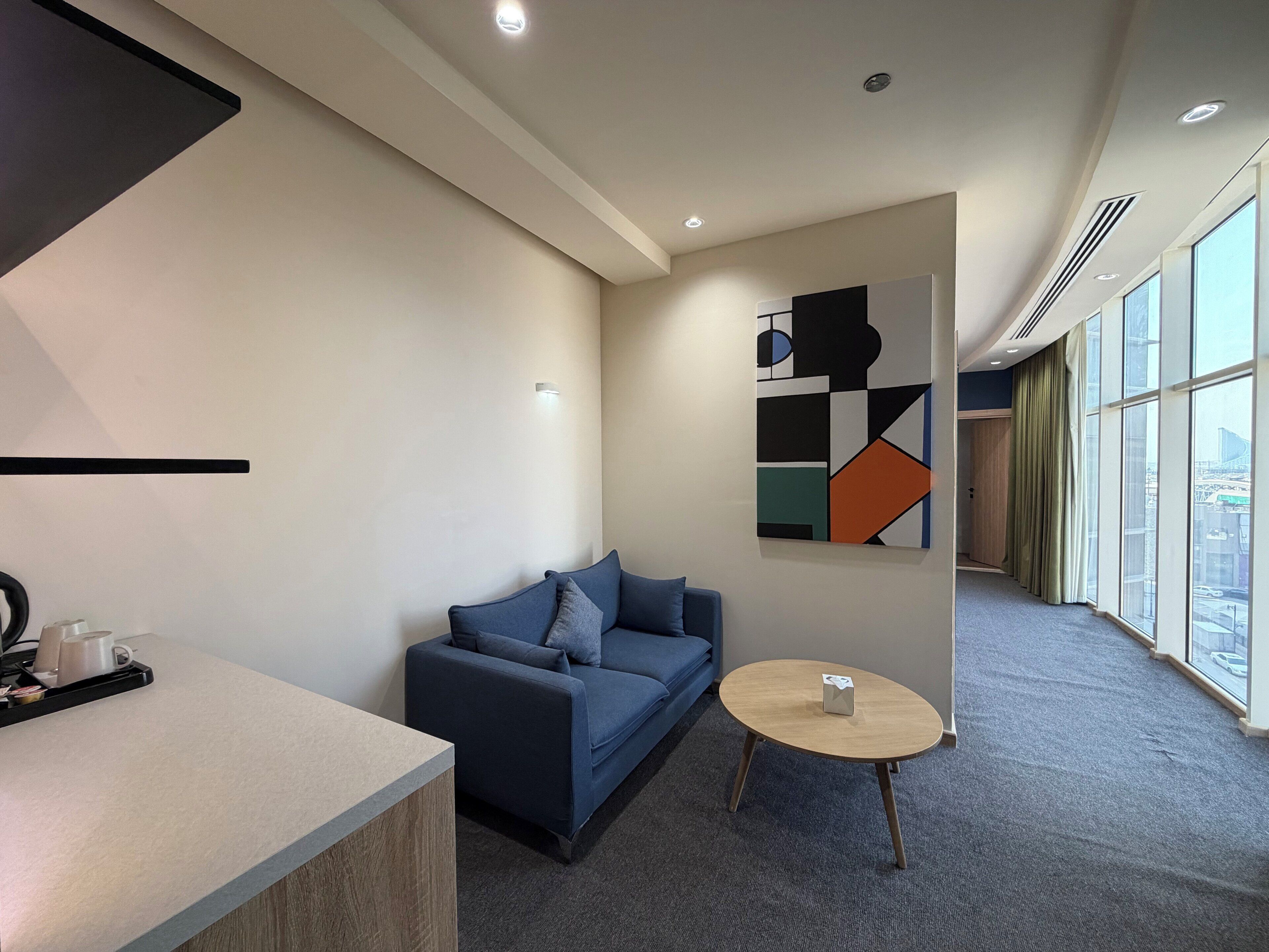 Ein modernes Hotelzimmer mit einer Couch, einem kleinen runden Tisch und einem großen Fenster mit Blick auf die Stadt.