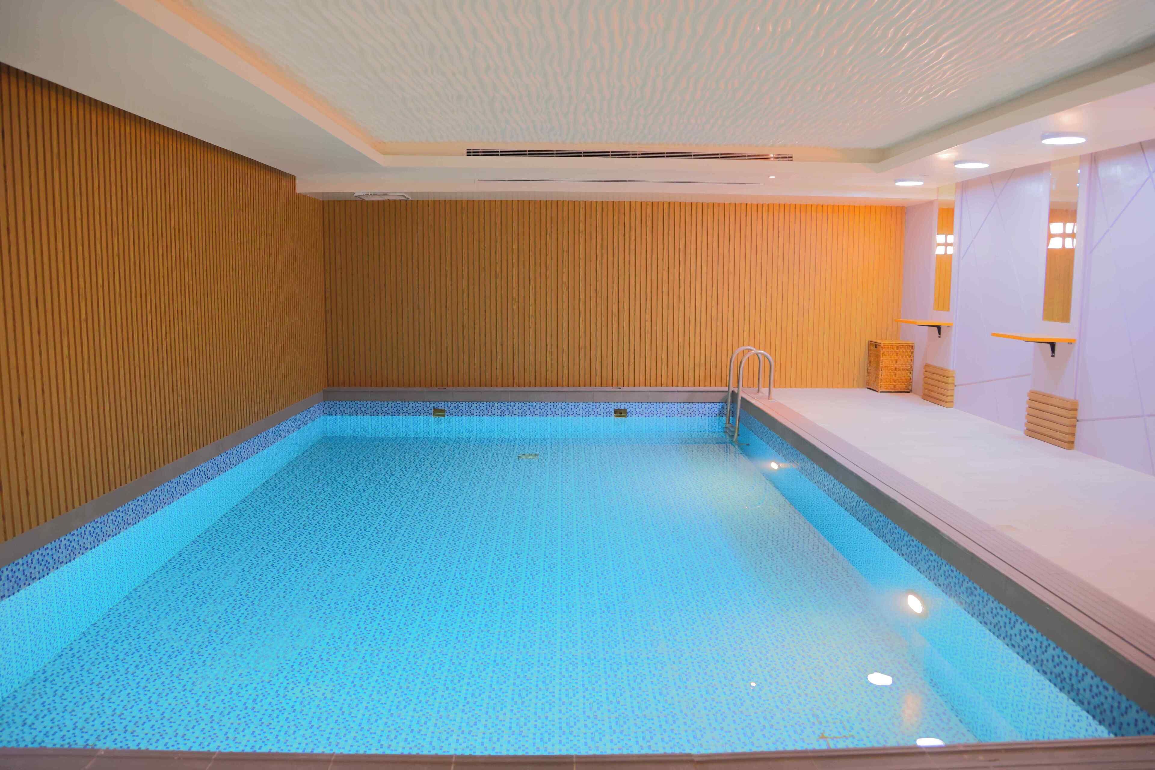 A large indoor swimming pool with a tiled floor and walls, surrounded by wooden paneling and a white ceiling.