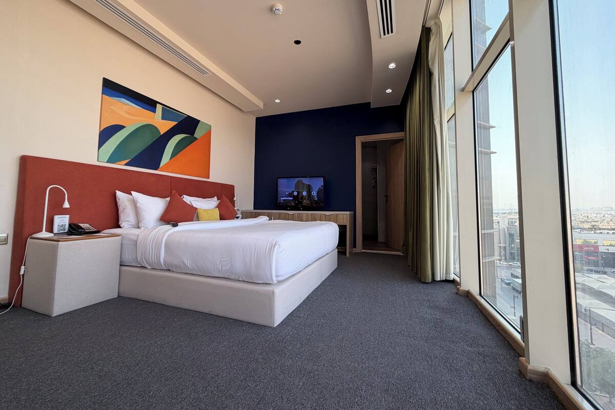 Hotelkamer met een groot bed, een bureau, een televisie en uitzicht op de stad door de ramen.