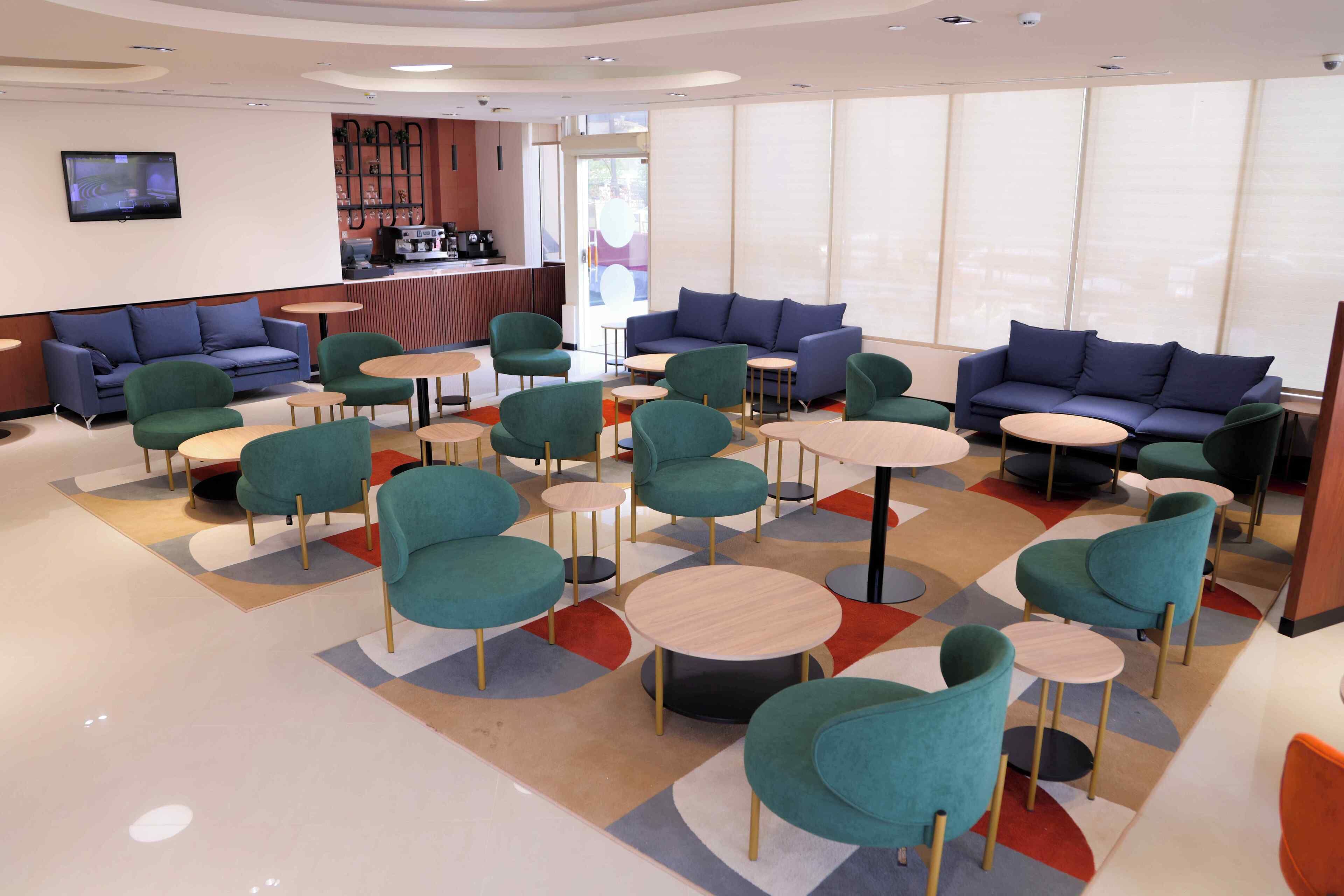 A modern lounge area with teal and blue sofas, round tables, and a coffee bar.